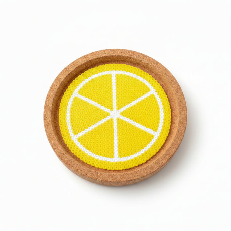 A round cork coaster featuring a printed yellow and white citrus slice design, shown on a brown wooden surface.