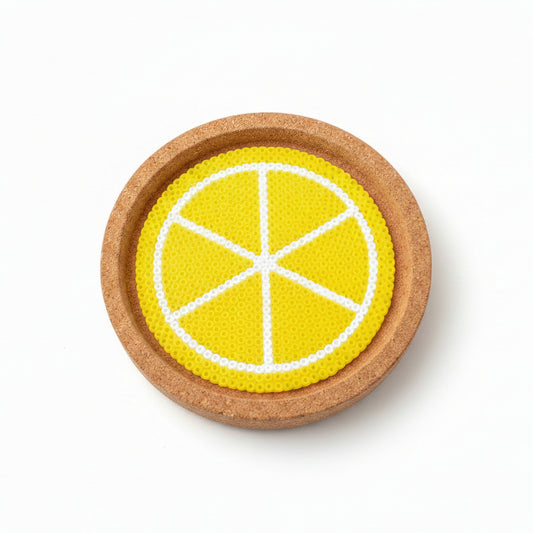 A round cork coaster featuring a printed yellow and white citrus slice design, shown on a brown wooden surface.