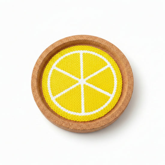 A round cork coaster featuring a printed yellow and white citrus slice design, shown on a brown wooden surface.